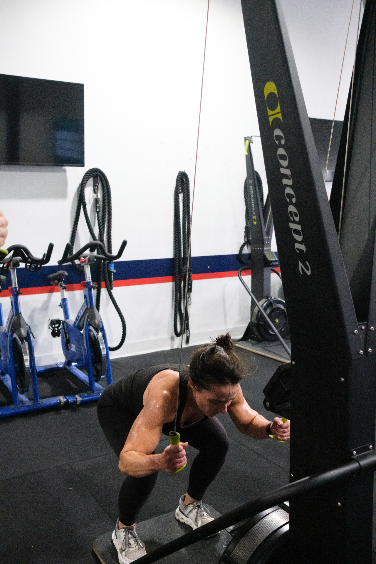Athlete pulling hard on a Concept2 SkiErg with battle ropes in background