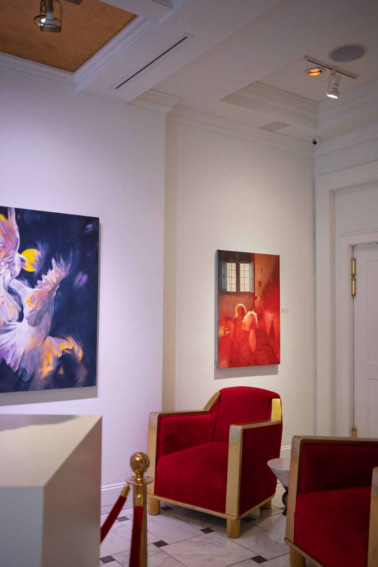 Red velvet armchairs and vibrant paintings inside a softly-lit Charleston gallery