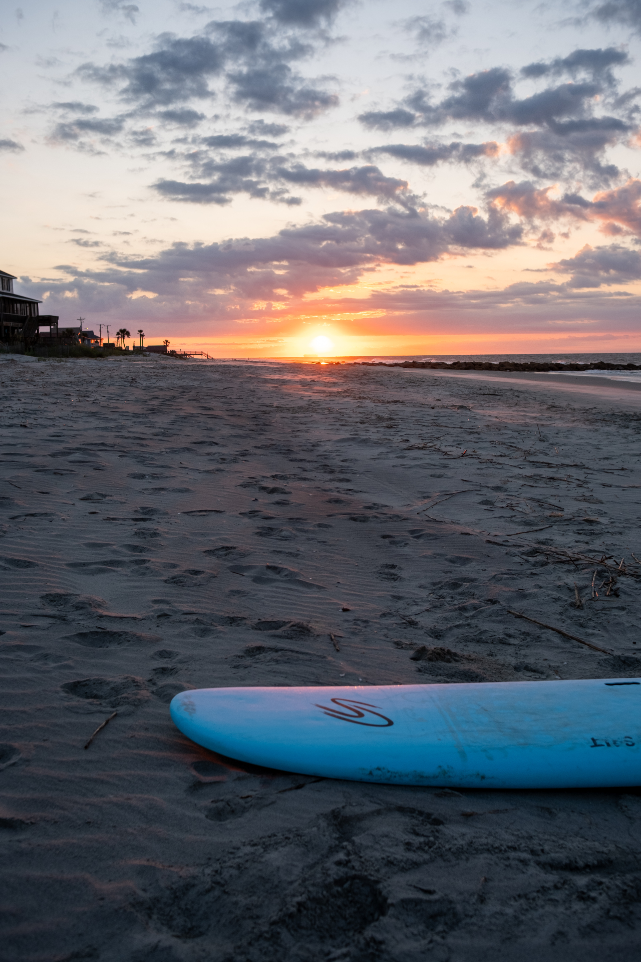 Blue longboard resting on Folly Beach sand at sunrise