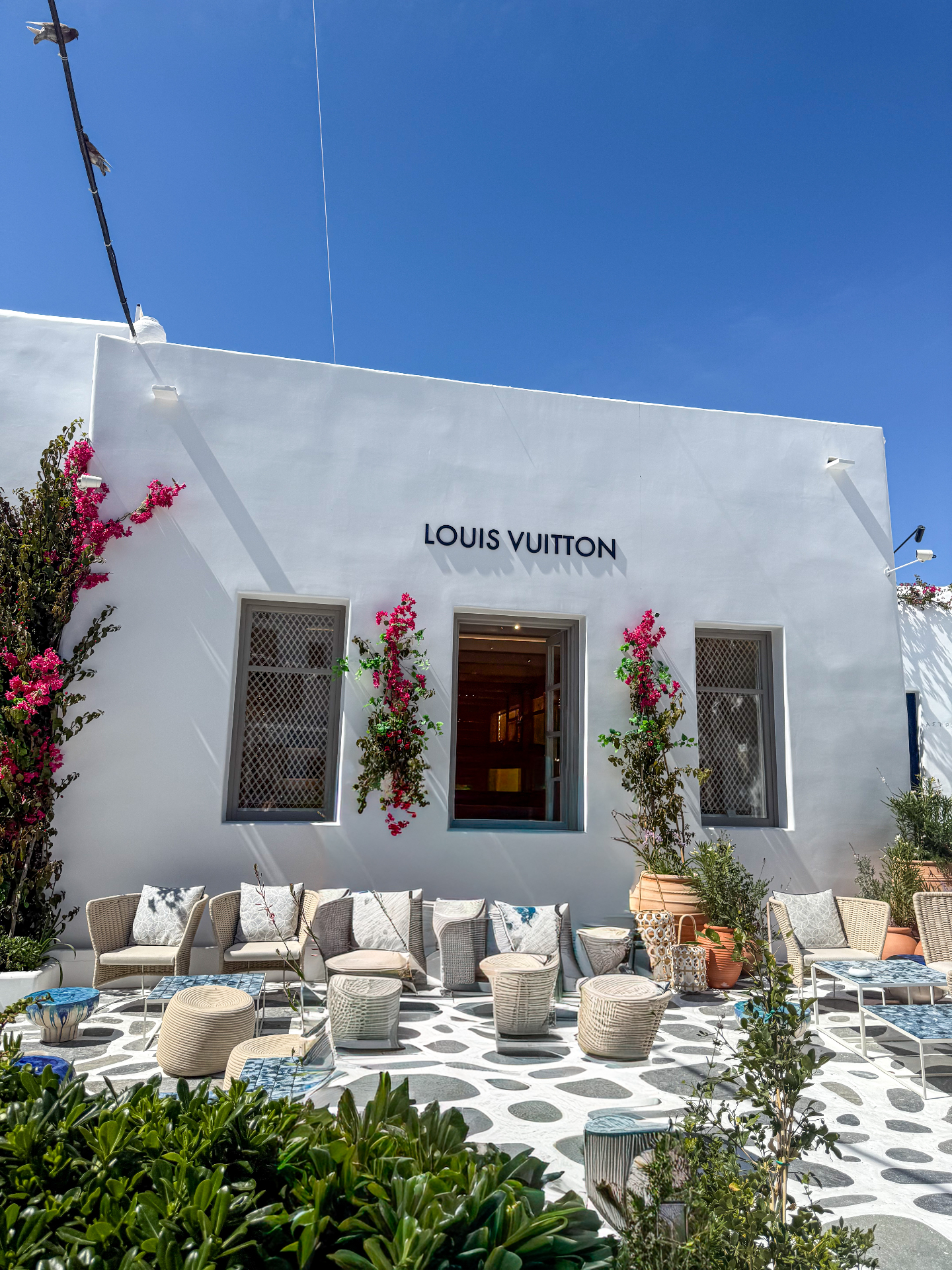 Whitewashed Louis Vuitton storefront with bright pink bougainvillea and cobalt sky in Mykonos