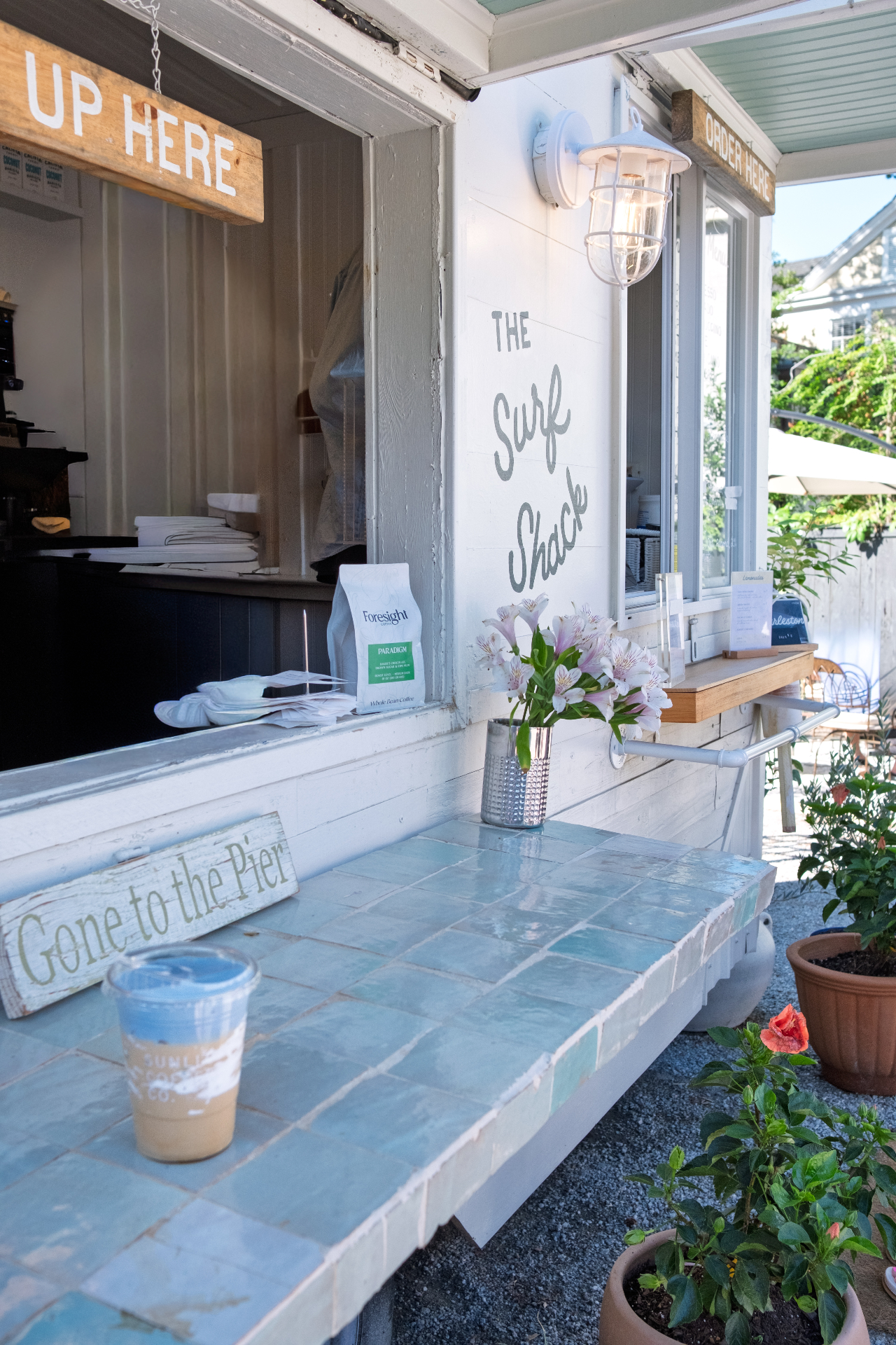 Soft blue surf shack counter window with flowers, coffee, and hand-painted lettering