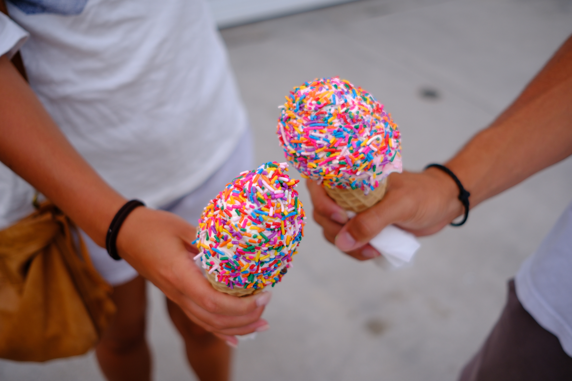 Two sprinkle-covered ice cream cones held in the sun