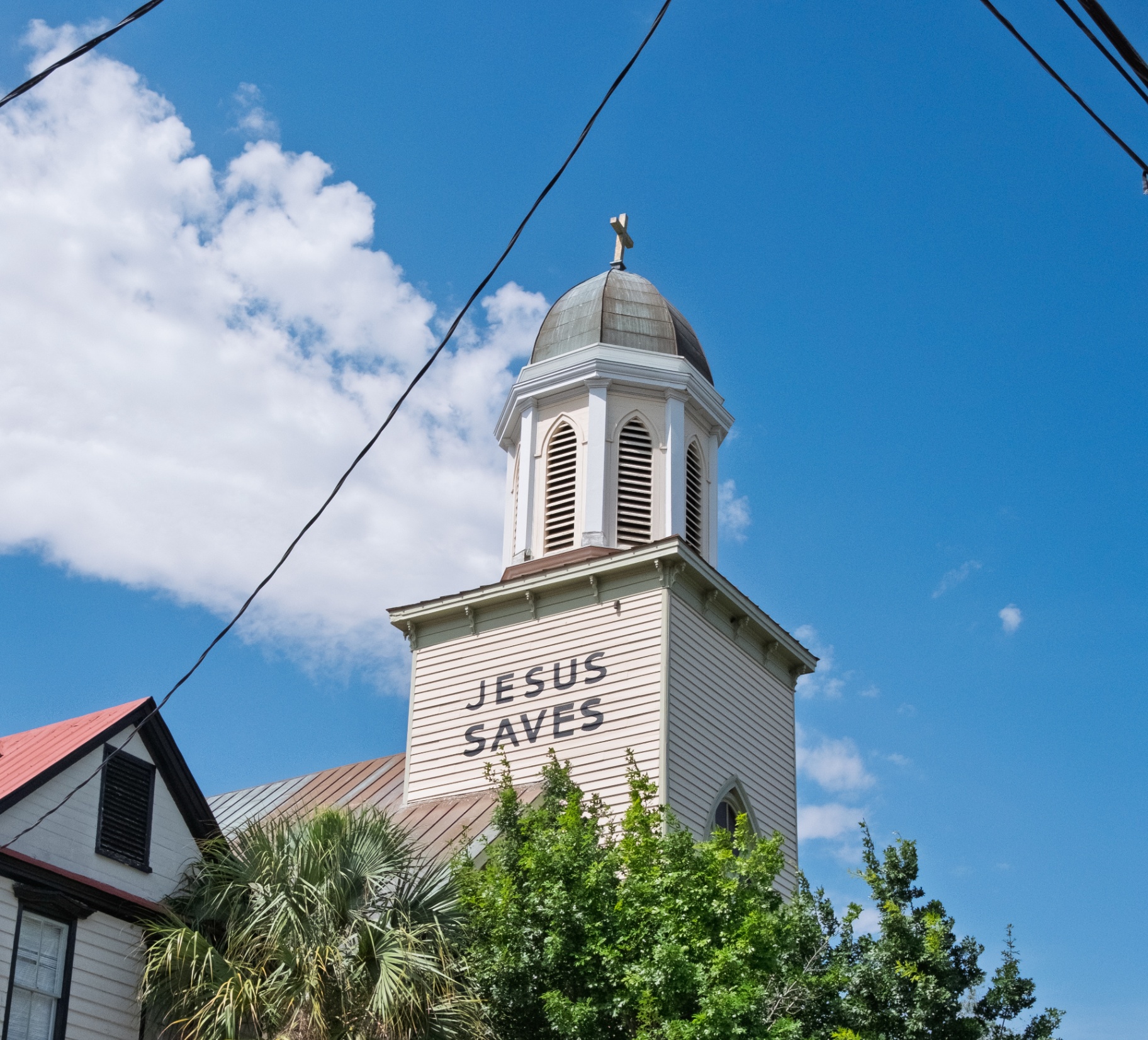 Charleston church steeple with 'Jesus Saves' sign under blue sky