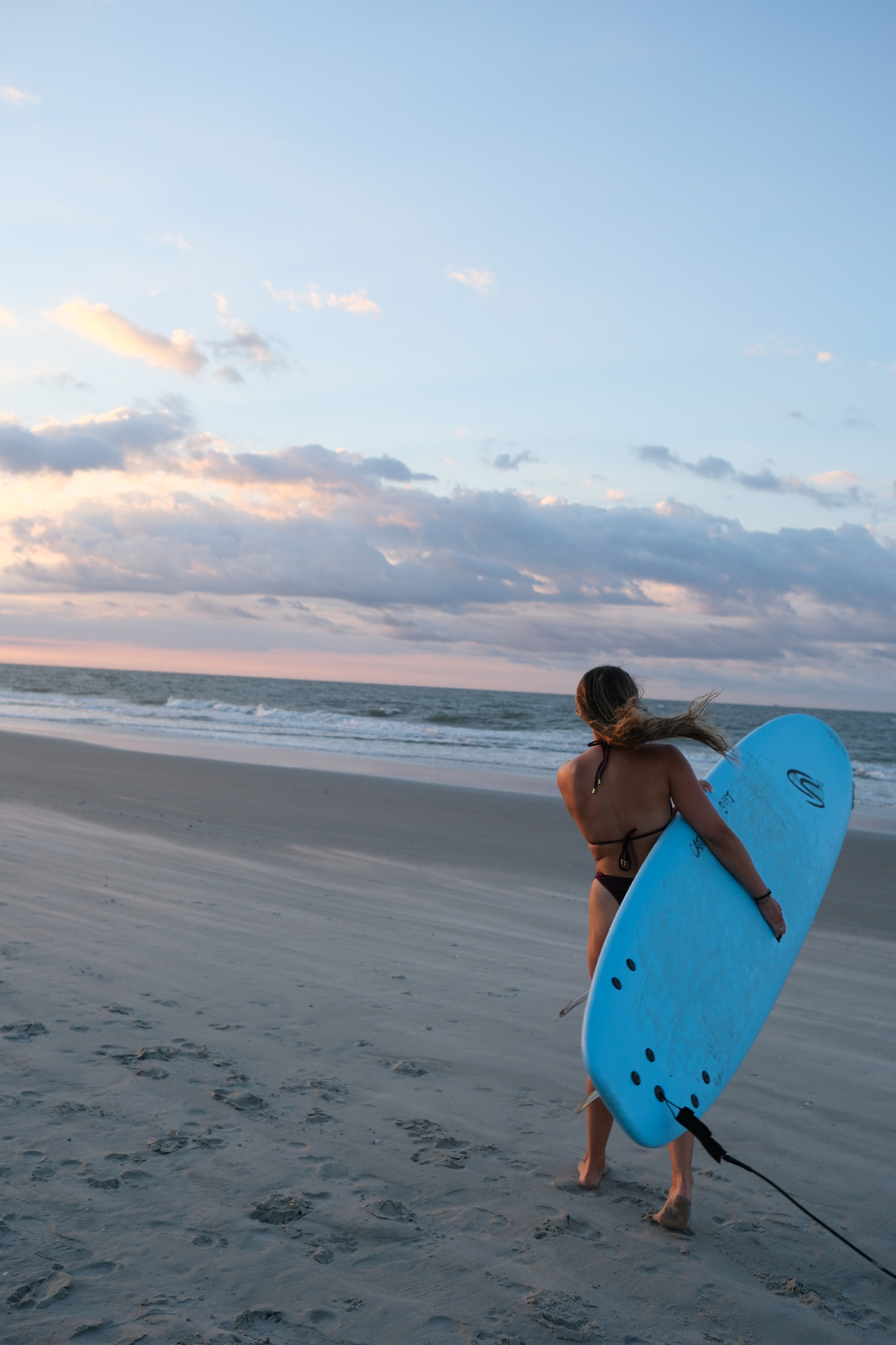 Surfer walking the shoreline at dusk with pastel sky