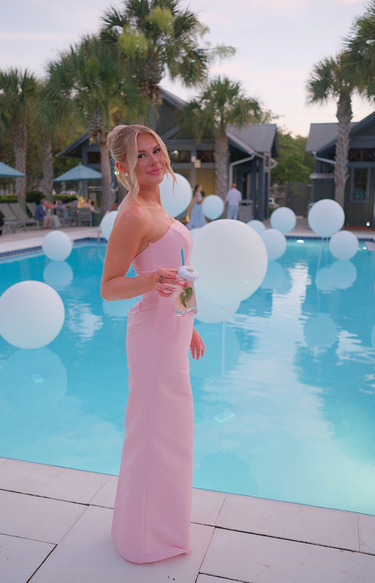 Portrait in a pink dress poolside at golden hour with floating balloons
