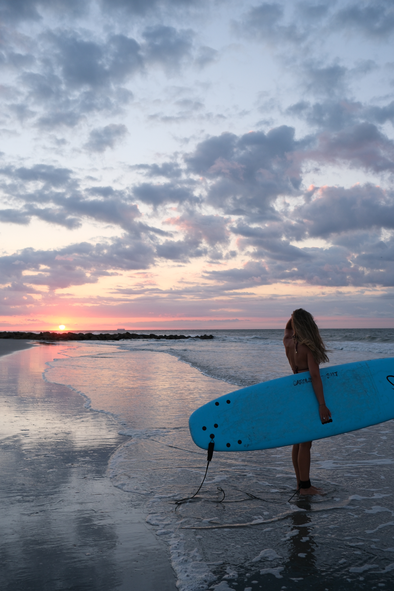 Surfer with blue longboard watching sunrise over the Atlantic