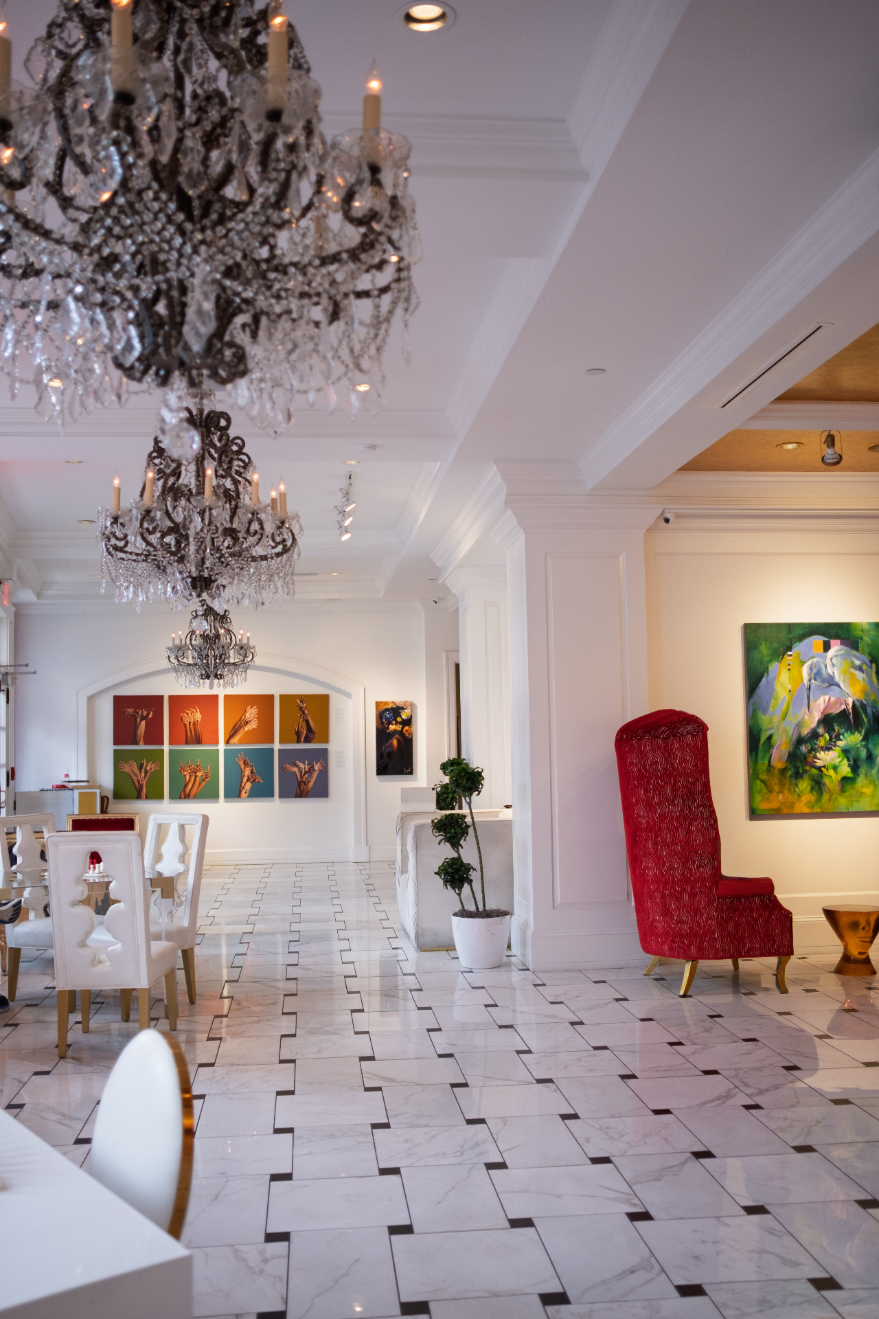 Crystal chandeliers above a marble-floor gallery hall with colorful hand paintings on the wall